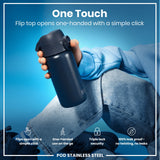 A dark-grey stainless steel water bottle is held; its flip top opens one-handed. The bottle is shown against a bright blue background. 