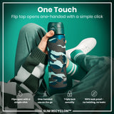 A teal and gray patterned water bottle is held; its flip top opens easily with one hand. The bottle is shown against a teal background, held by a person wearing a green sweater. 