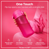 A pink water bottle is being held; its flip top opens easily with one hand. The bottle rests on a pink surface. 