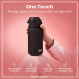 A black ION8 water bottle is held; its flip top opens one-handed. The bottle rests on pink fabric against a pink background; text highlights its features. 