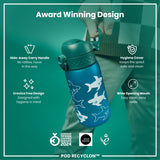 A blue water bottle, with a teal lid and sharks printed on it, is being held. It features a hide-away handle, hygiene cover, and wide mouth. The bottle is an award-winning design.